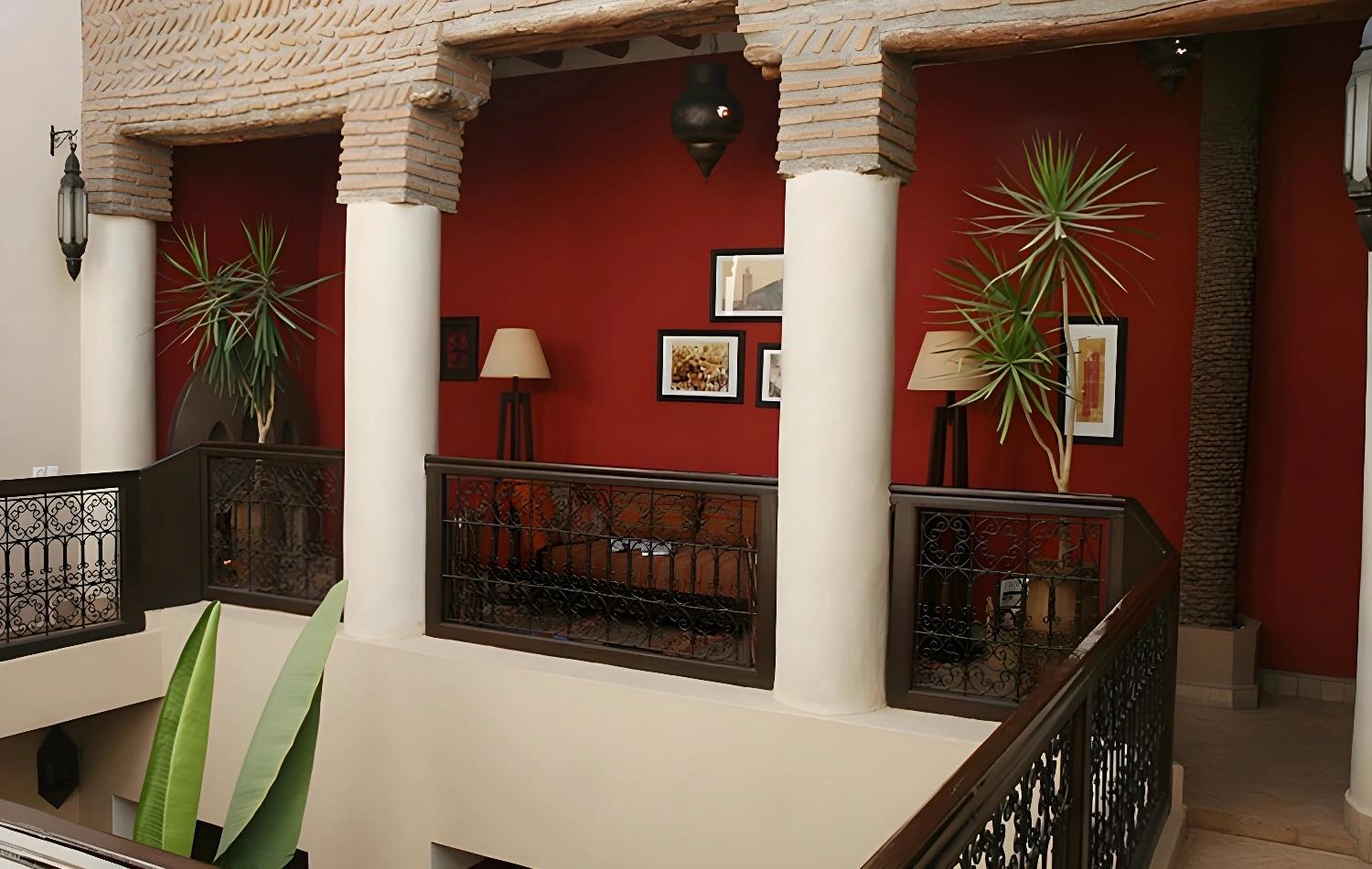Balcon du Riad Boussa avec des colonnes blanches et un mur rouge.
