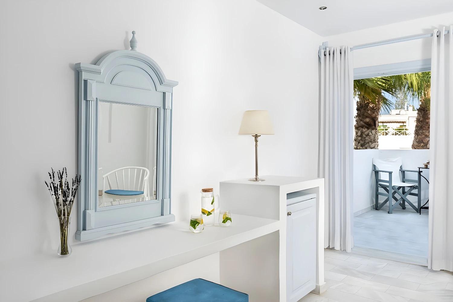 Intérieur lumineux d'une chambre avec miroir et terrasse au Santorini Kastelli.