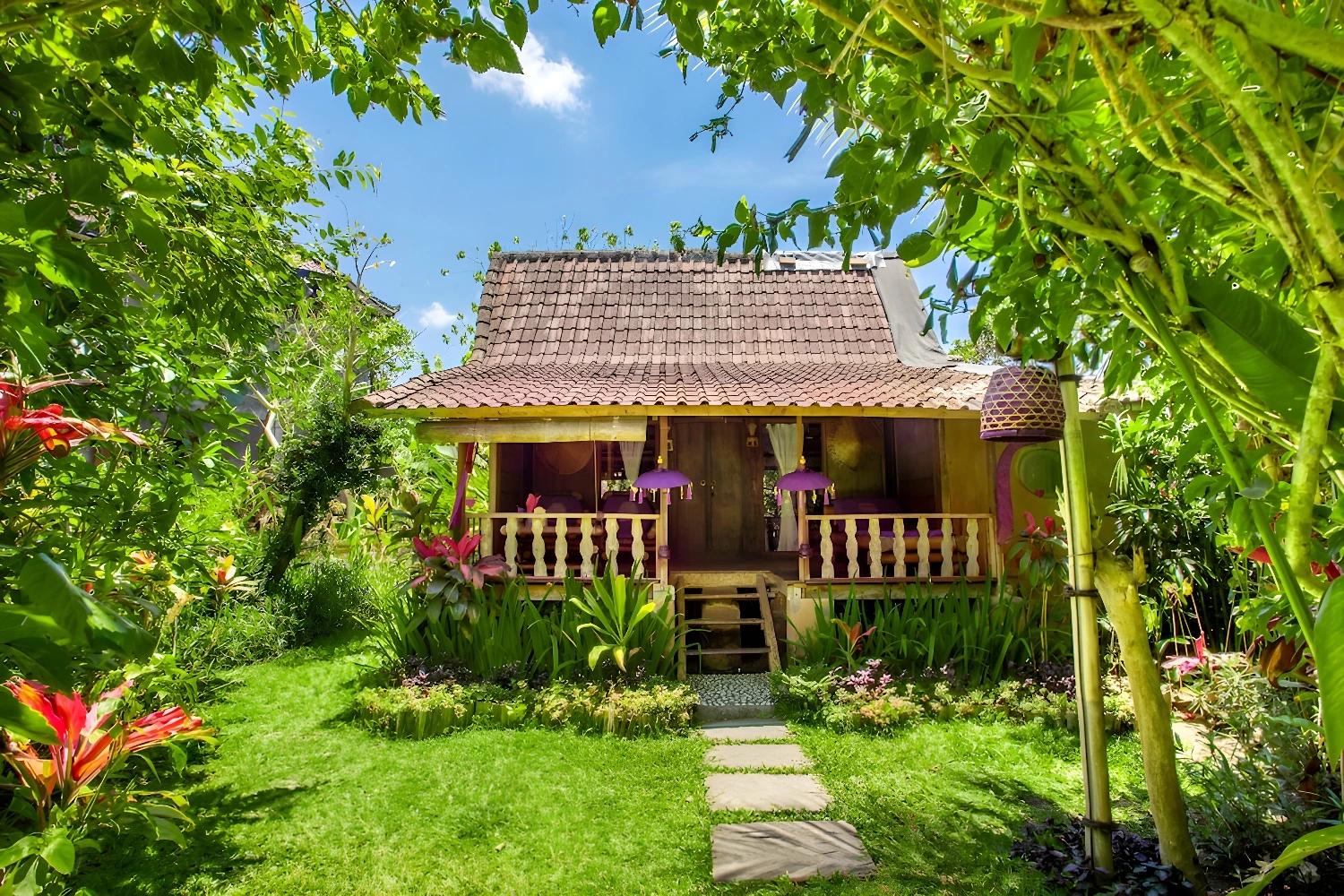 Façade du Swasti Eco Cottage avec jardin verdoyant et fleurs colorées.