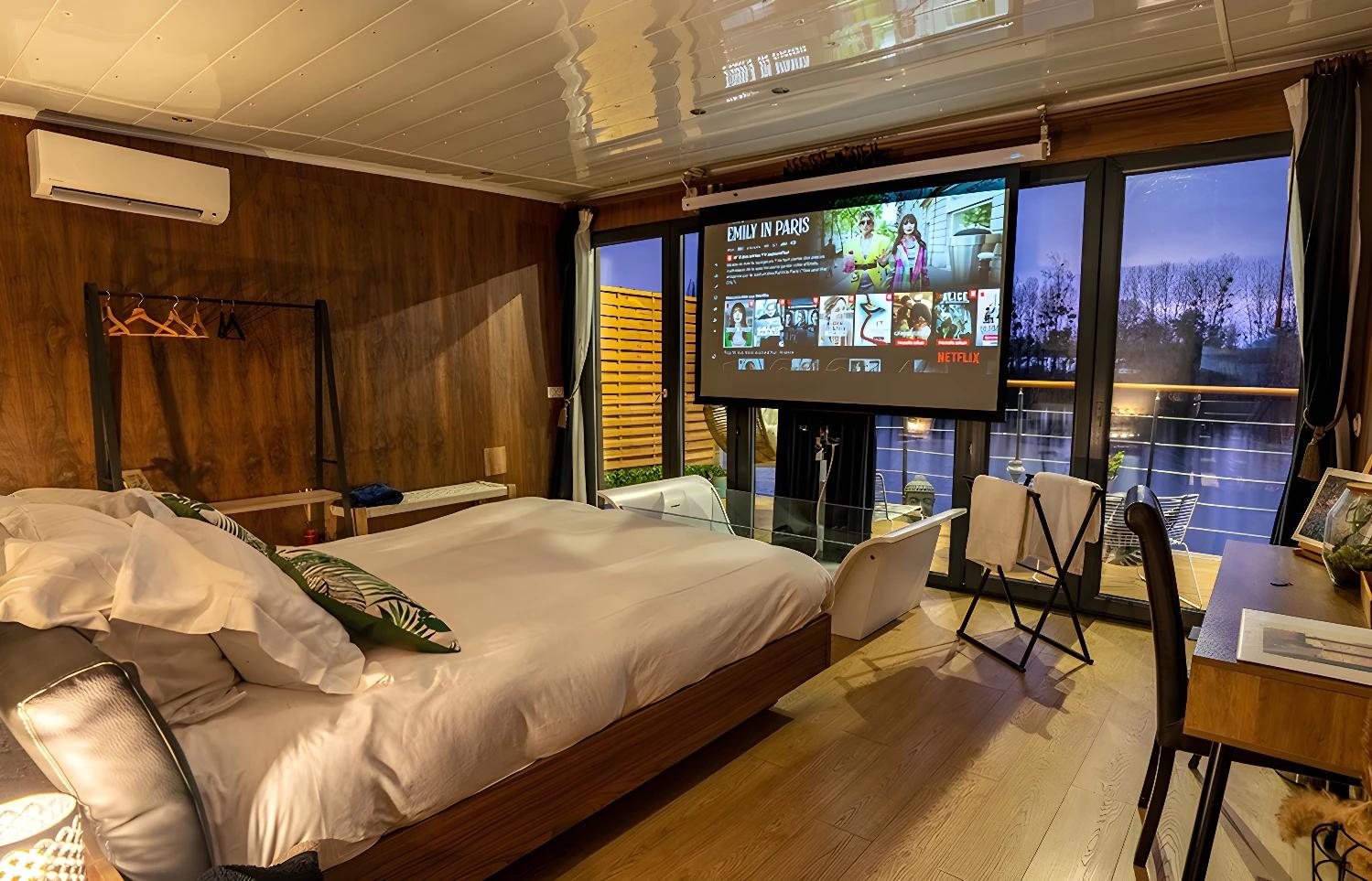 Intérieur de L'Escale Royale Port Ilon avec un lit et un écran de projection.