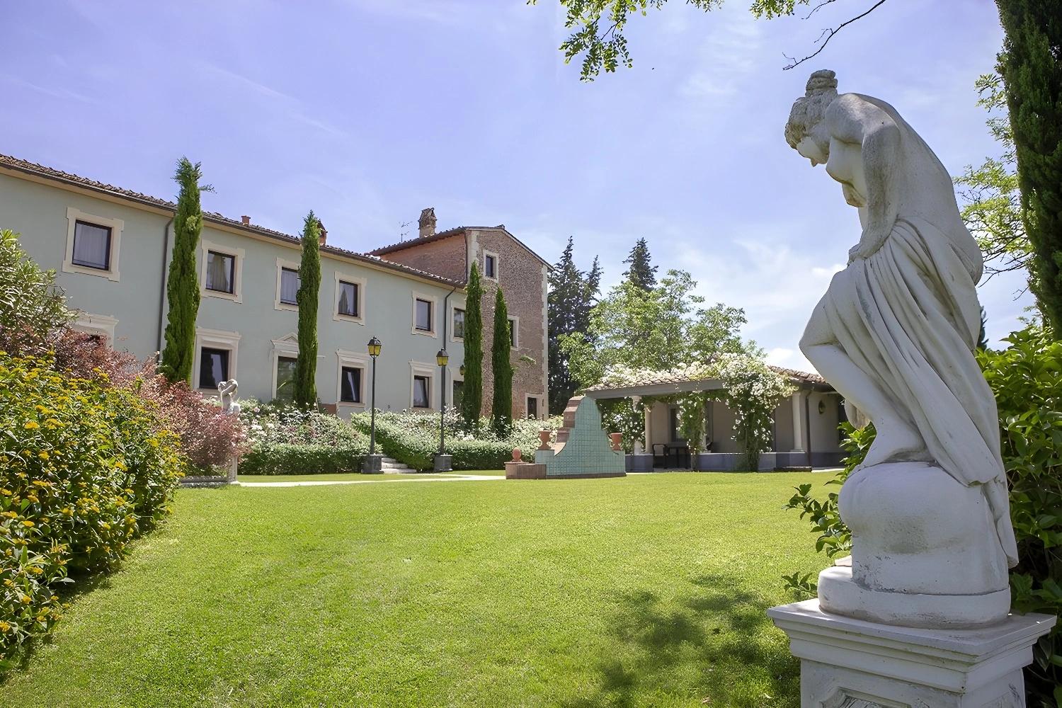 Jardin du Relais Sassa al Sole avec statue et bâtiment principal en arrière-plan.