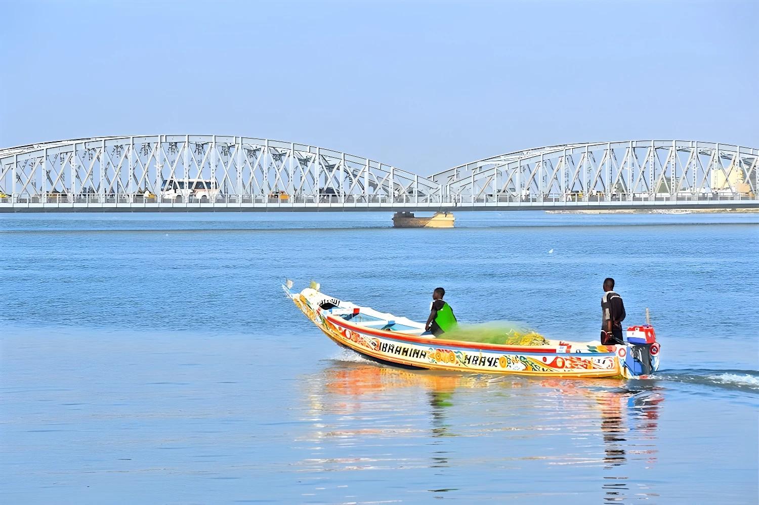 Pirogue colorée sur le fleuve avec un pont en arrière-plan à Saint-Louis.