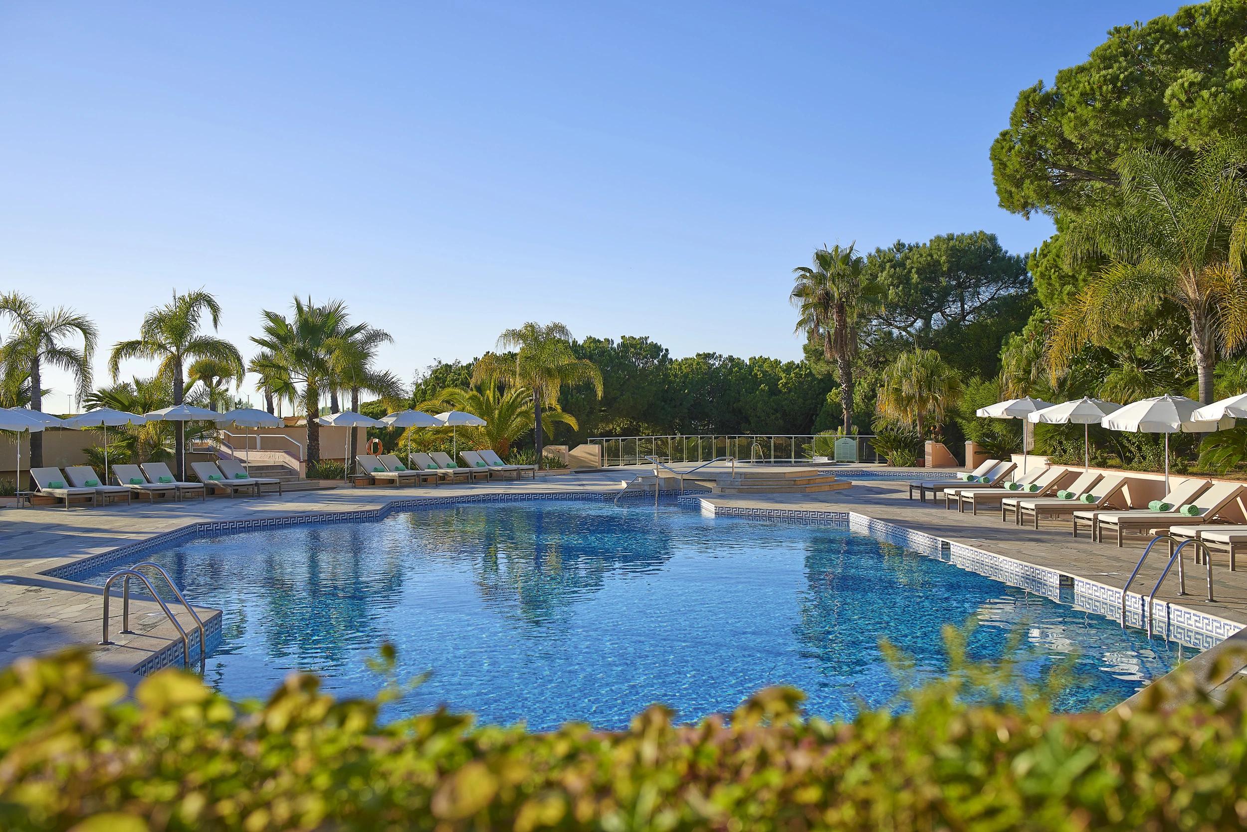Piscine extérieure de l'Hotel Quinta Do Lago entourée de chaises longues et de palmiers.