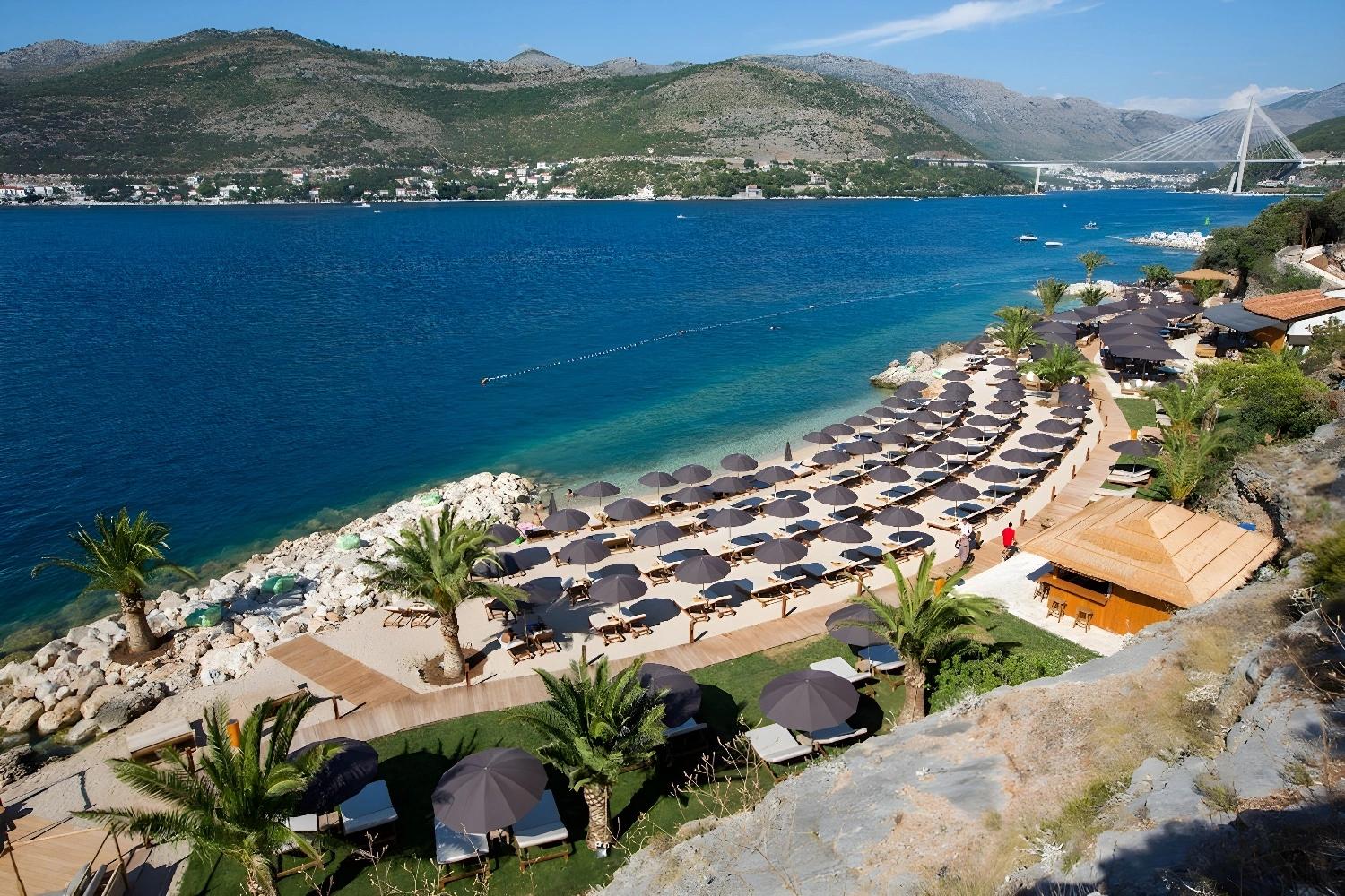 Vue aérienne de la plage privée du Valamar Collection Dubrovnik President avec parasols et chaises longues.