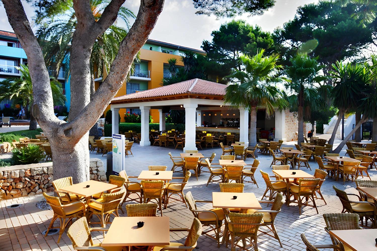 Terrasse extérieure du restaurant de l'Ôclub Experience Occidental Minorque entourée de verdure.