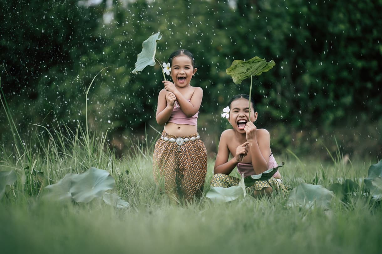 Deux enfants souriants jouant dans un parc à Bali, avec des feuilles comme parapluies.
