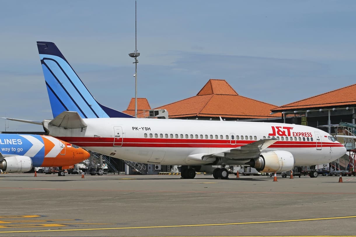 Aéroport Ngurah Rai avec un avion J&T Express au sol, et toits traditionnels balinais en arrière-plan