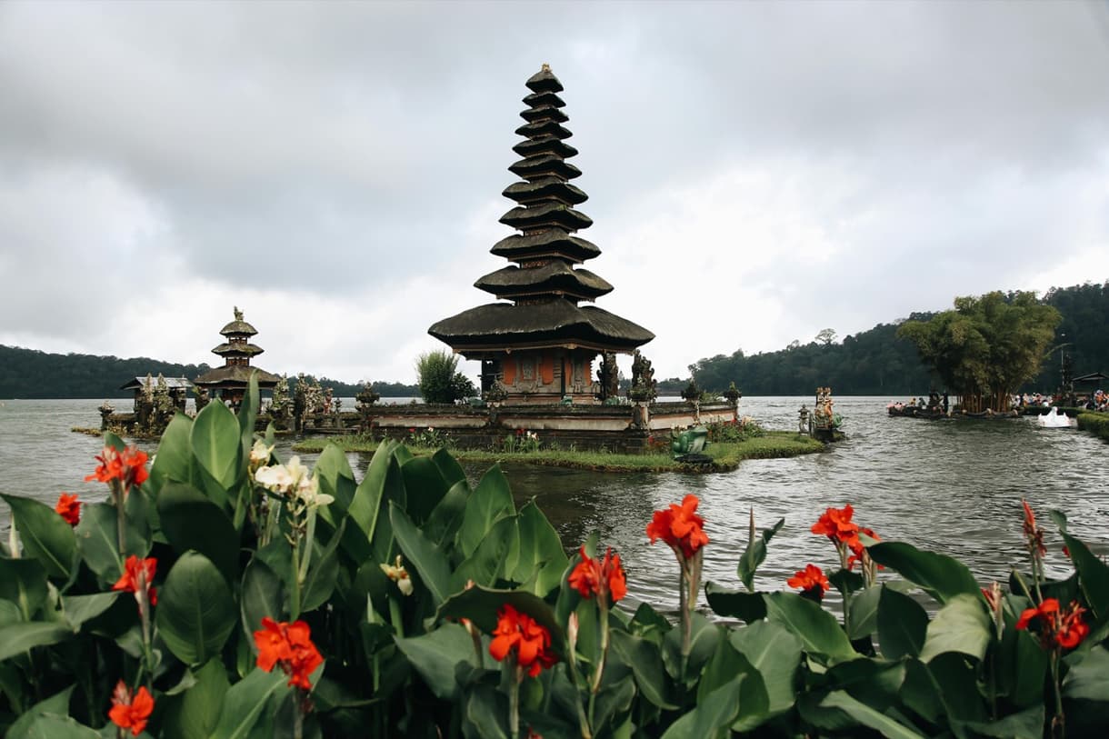 Temple du Lac Bratan à Bedugul, entouré de fleurs au premier plan et de montagnes en arrière-plan.