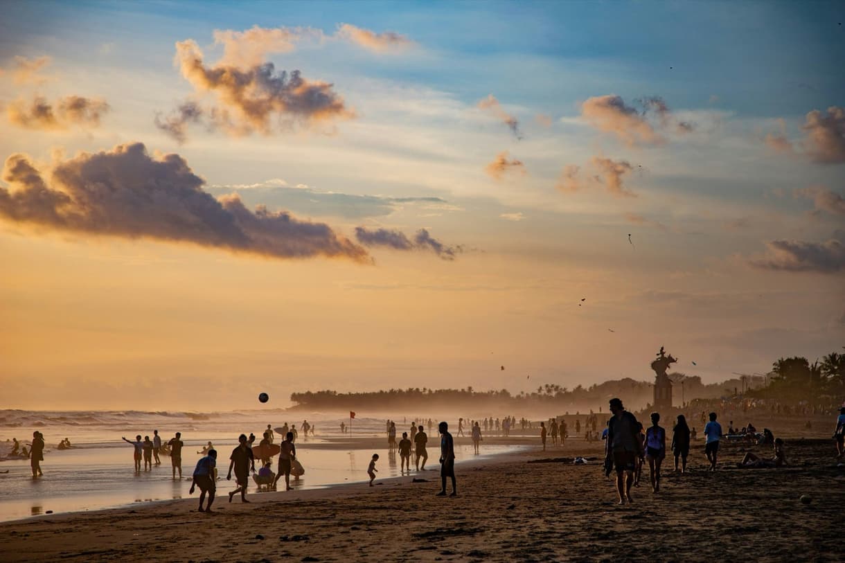 Plage animée à Canggu au crépuscule, avec des silhouettes de personnes se baignant et jouant.