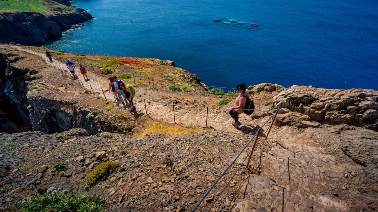 Via ferrata sur un sentier rocheux surplombant la mer, avec un groupe de personnes en randonnée.