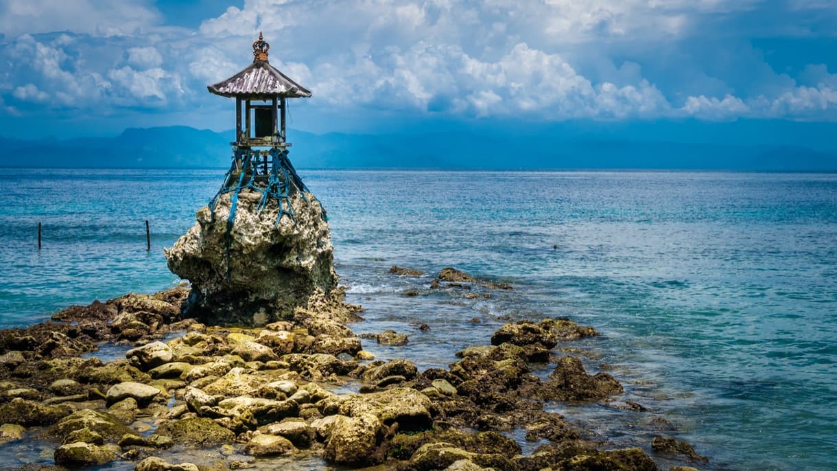 Temple sur un rocher face à la mer à Nusa Penida, ciel bleu avec nuages