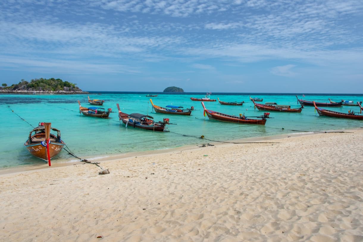 Plage aux eaux turquoise et bateaux traditionnels en Thaïlande