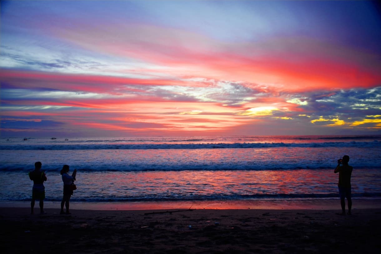 Coucher de soleil sur Dreamland Beach, silhouettes de personnes admirant l'horizon, vagues paisibles.