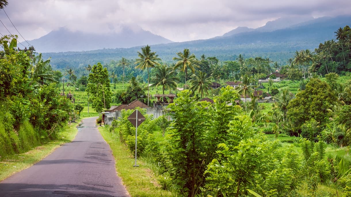 Route rurale à Bali entourée de végétation luxuriante et de montagnes en arrière-plan