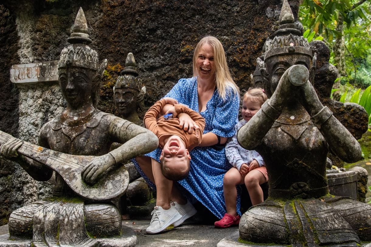 Une mère s'amuse avec ses deux enfants près de sculptures à Bali, ambiance joyeuse et familiale.