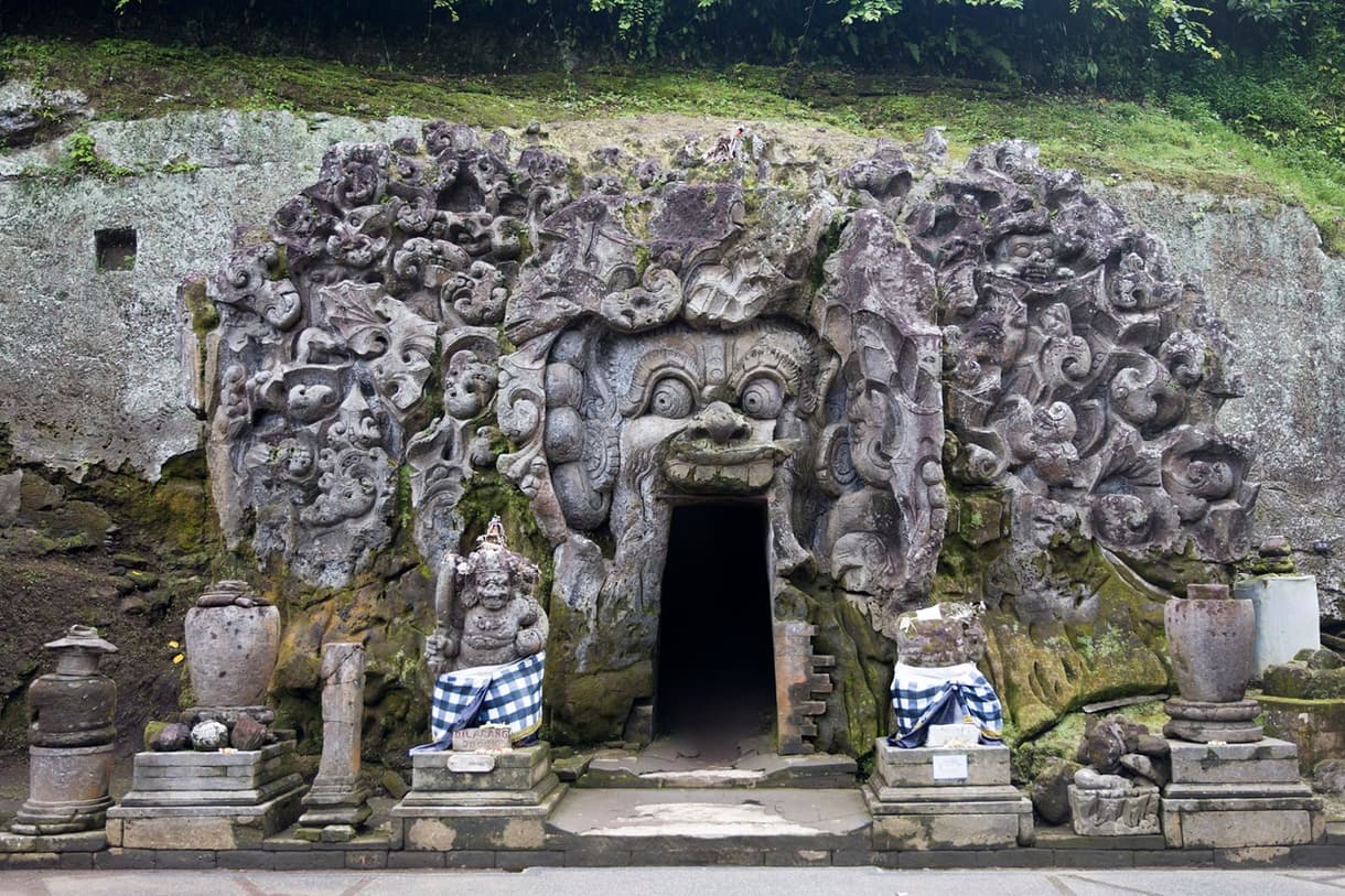 Entrée ornée de sculptures de la Grotte de l'Éléphant à Bali, entourée de statues et d'objets sacrés.