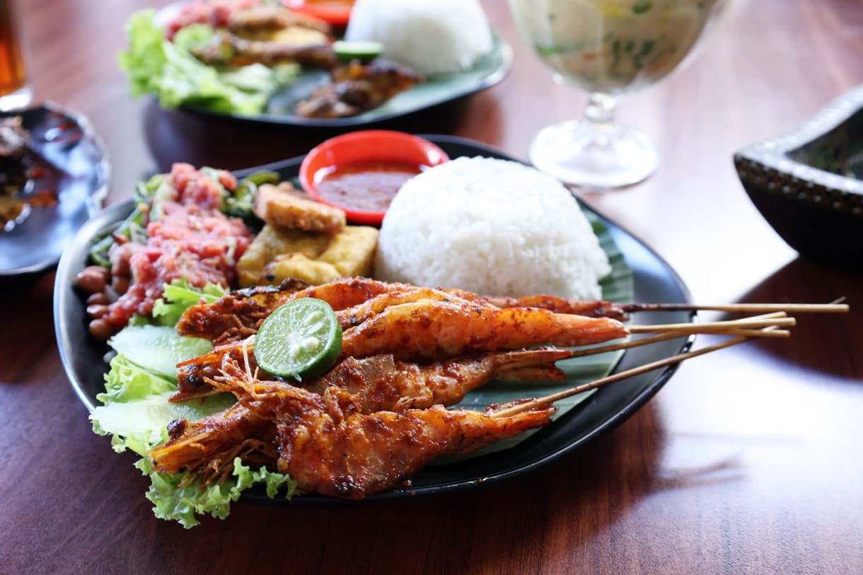 Crevettes grillées épicées accompagnées de riz, salade et sauce, typique de Bali.