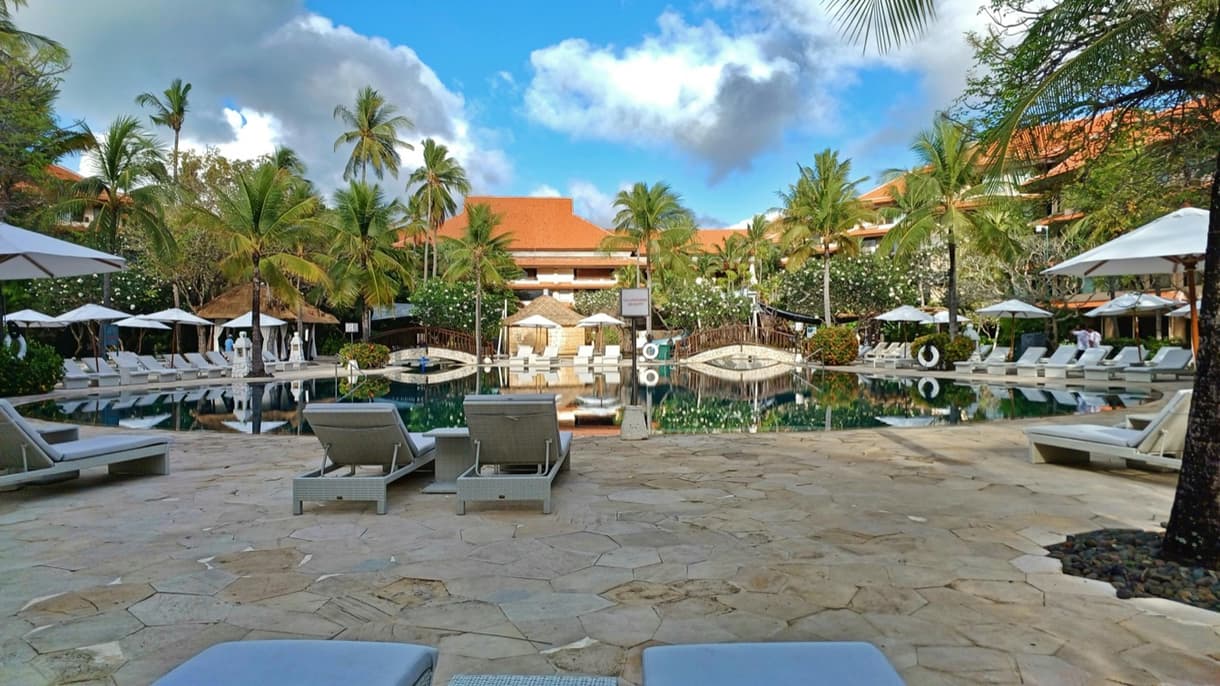 Piscine d'un hôtel de luxe à Bali, entourée de palmiers et chaises longues