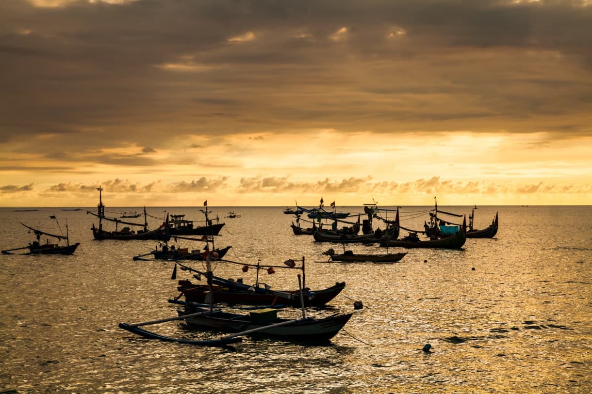 Coucher de soleil sur la plage de Jimbaran, bateaux de pêche en silhouette sur l'eau