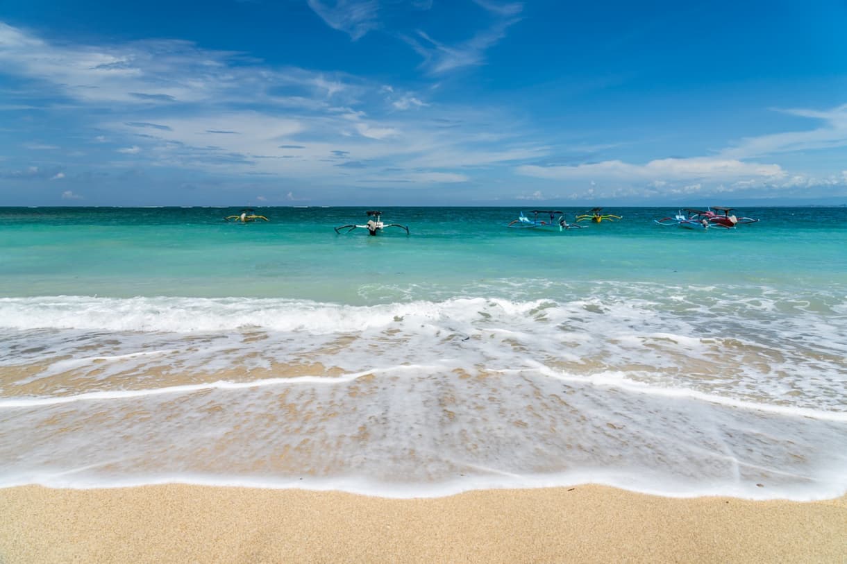 Kuta Beach à Bali avec des surfeurs et des bateaux colorés sur l'eau turquoise
