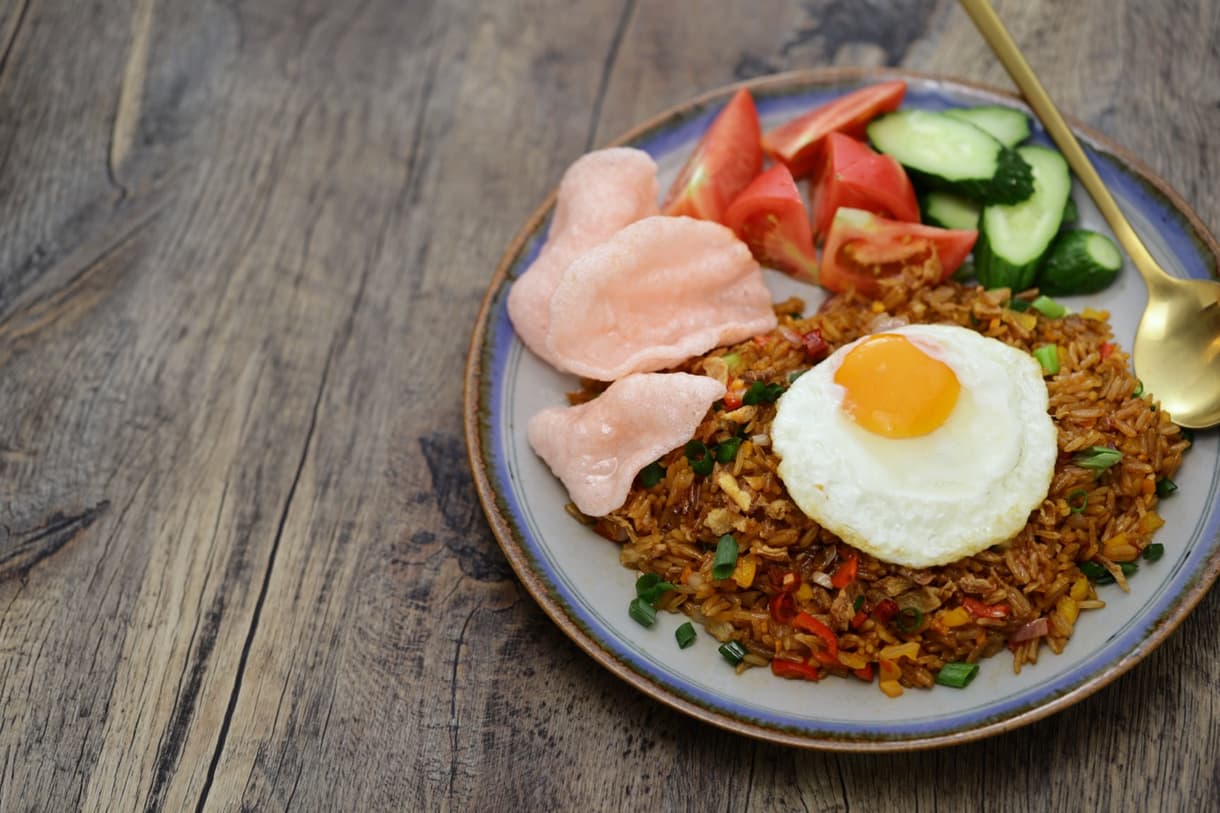 Nasi Goreng, riz frit indonésien, avec œuf au plat et garnitures de légumes, sur une table en bois