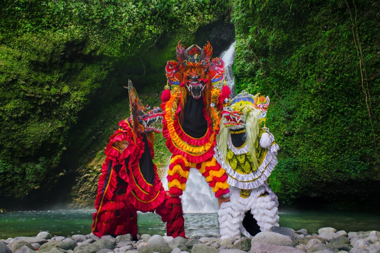 Trois danseurs traditionnels balinais en costumes colorés devant une cascade, célébrant le jour du silence.