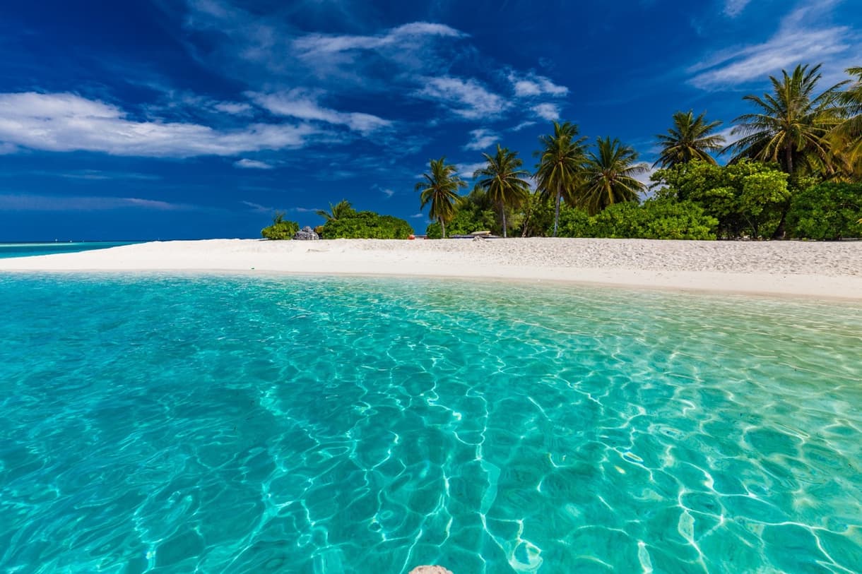 Plage de sable blanc aux Maldives, eau turquoise et ciel bleu, ambiance tropicale