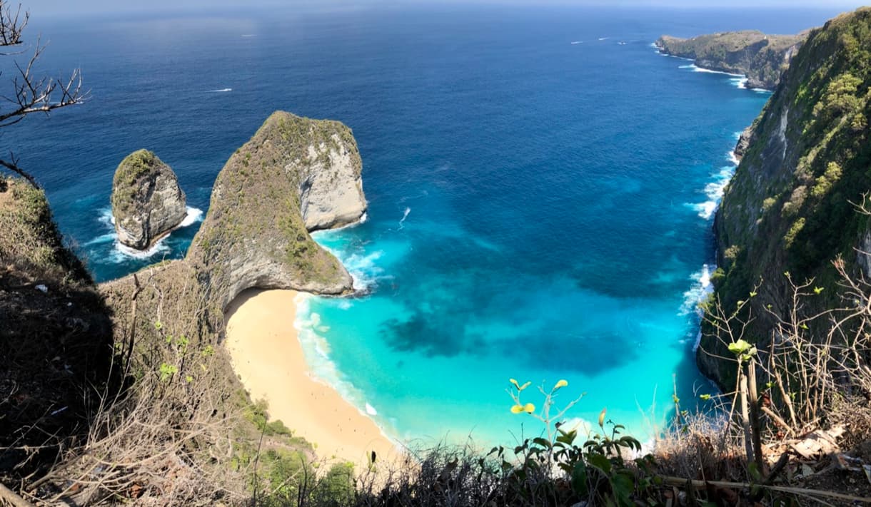 Plage iconique de Bali avec des falaises verdoyantes et une mer turquoise, illuminée par le soleil