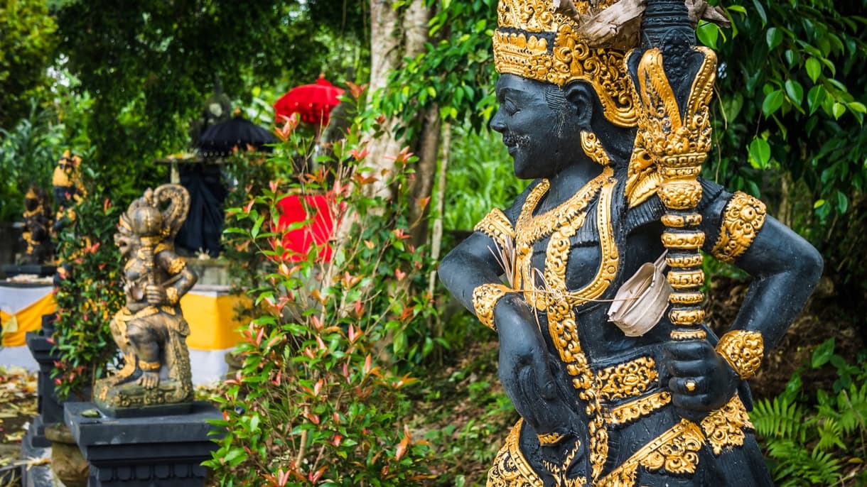 Entrée d'un temple balinais avec une statue de gardien colorée, entourée de verdure.