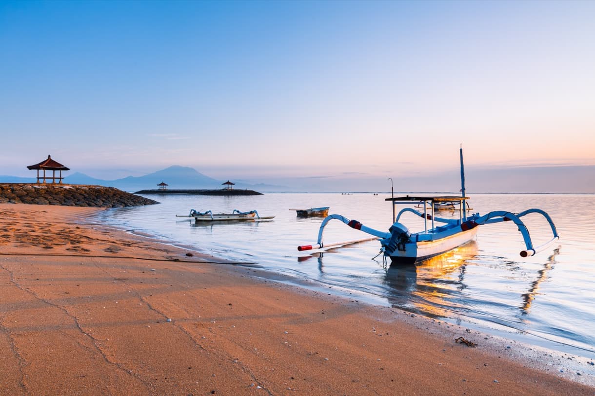 Sanur, plage paisible à l'aube avec des bateaux traditionnels et un paysage montagneux en arrière-plan
