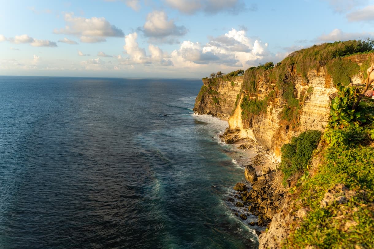 Cliffs of Uluwatu overlooking the ocean, with vibrant waves lapping at the rocky coastline.