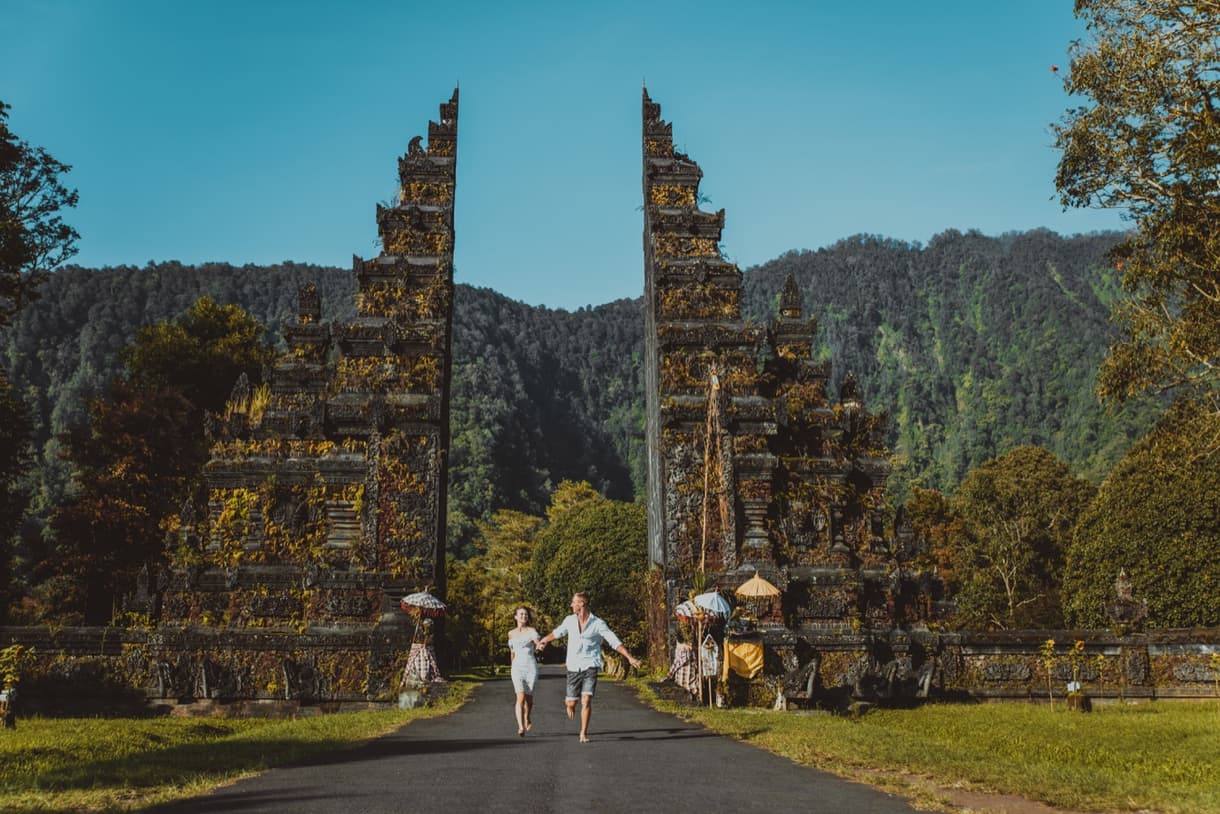 Couple se tenant la main devant la porte de Handara à Bali, entouré de montagnes verdoyantes