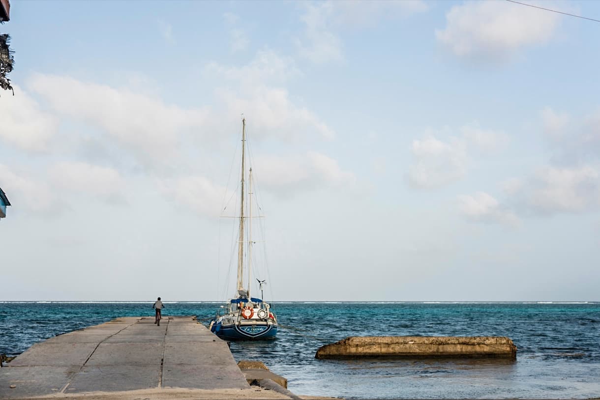 San Pedro, Ambergris Caye : un quai en béton avec un voilier, eau turquoise et ciel dégagé