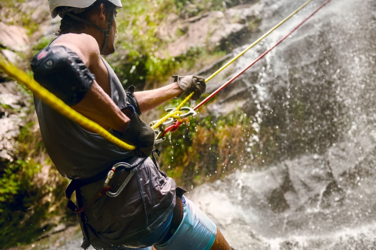 Rappel le long d'une cascade, avec un homme en équipement de sécurité, au cœur de la nature verdoyante