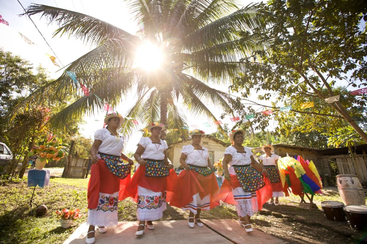 Danseurs en costumes traditionnels au Belize, entourés de palmiers et de décorations colorées.