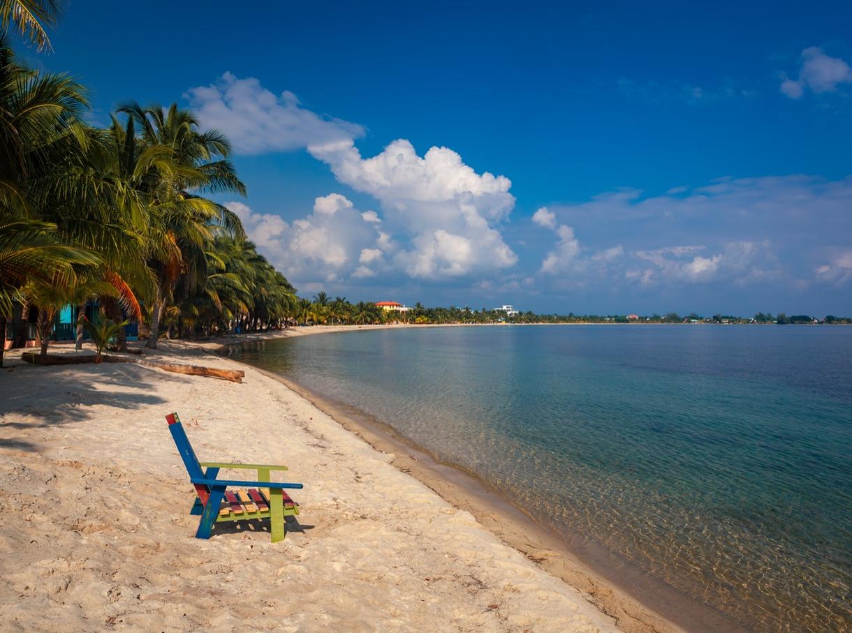 Plage de Placencia avec chaises colorées, palmiers et eau cristalline sous un ciel bleu