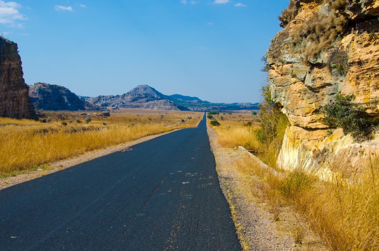 Route asphaltée traversant un paysage désertique à Madagascar, entourée de collines et d'herbes sèches