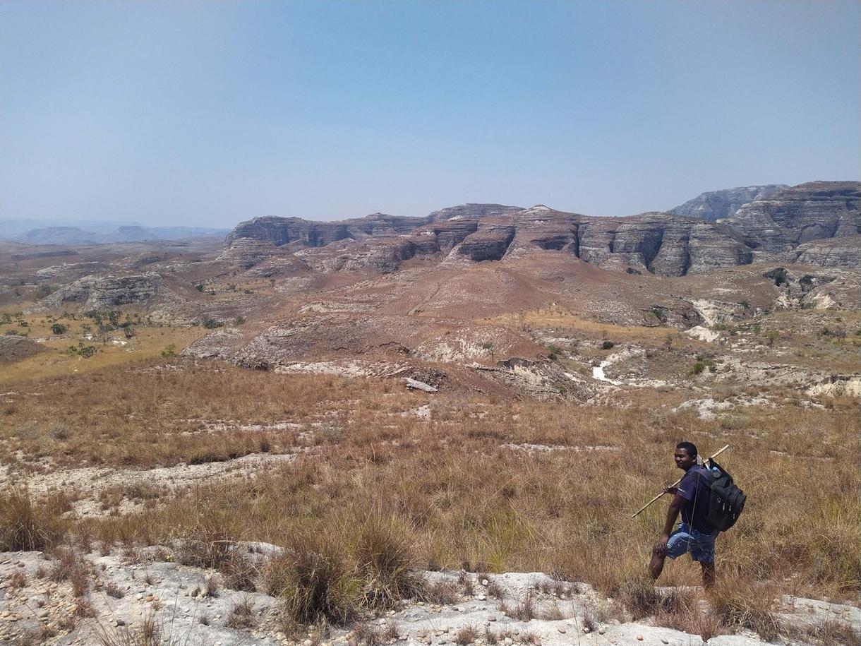 Paysage aride avec collines et un marcheur portant un sac à dos dans le Sud Sauvage de Madagascar.