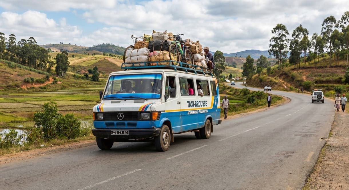 Taxi-brousse sur route malgache avec chargement sur le toit, panorama rural en arrière-plan.