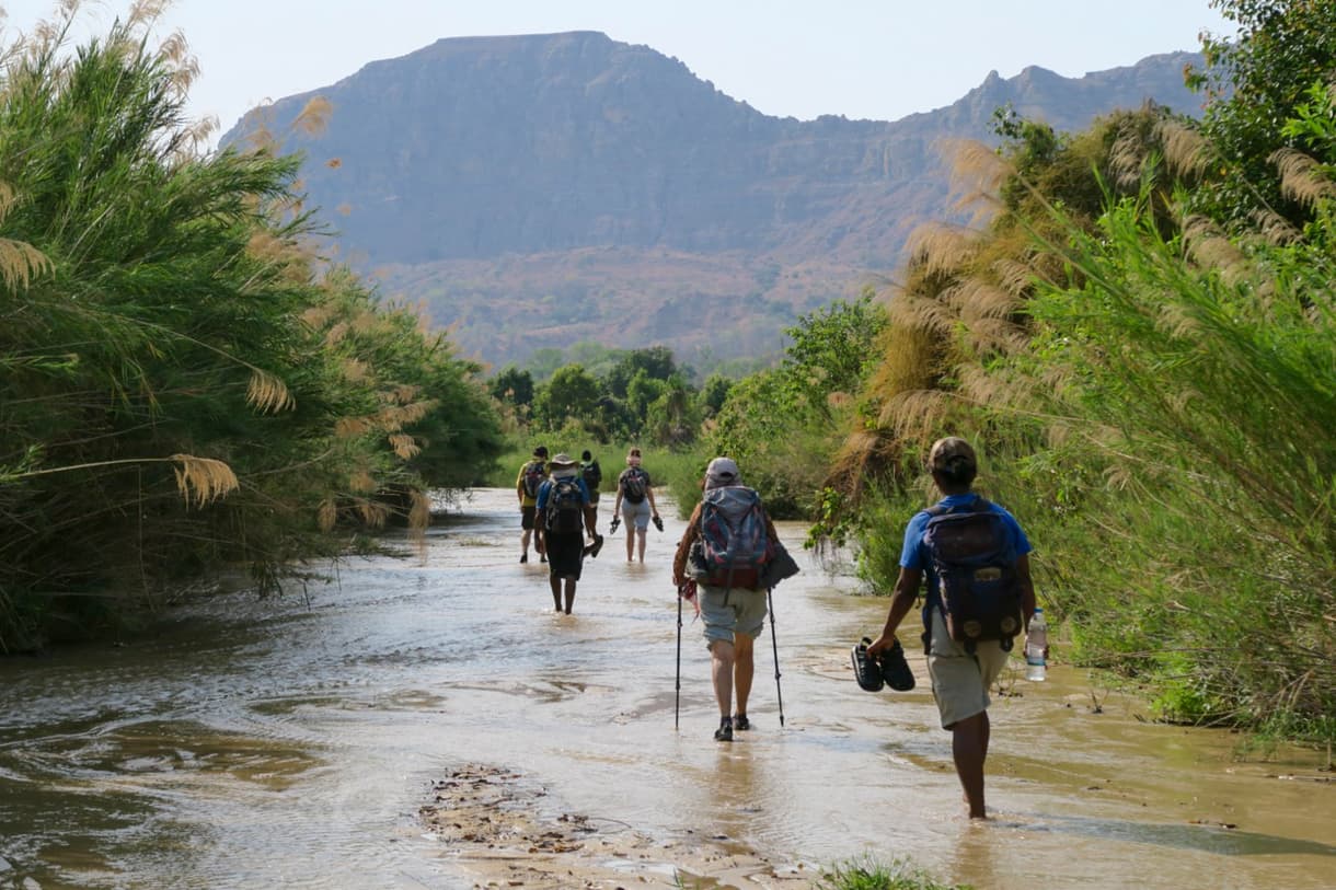 Trek au bord d’une rivière, avec des randonneurs et des montagnes en arrière-plan.