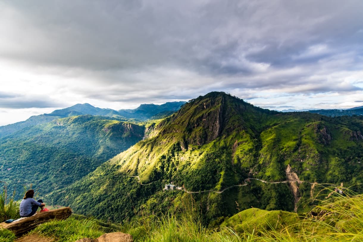 Vue panoramique d'Adam's Peak, montagne sacrée du Sri Lanka, avec un pèlerin contemplant le paysage verdoyant.