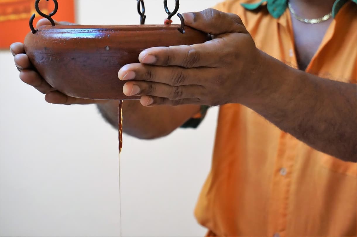 Pratique ayurvédique : infusion d'huile coulant d'un bol en terre cuite, promesse de bien-être.
