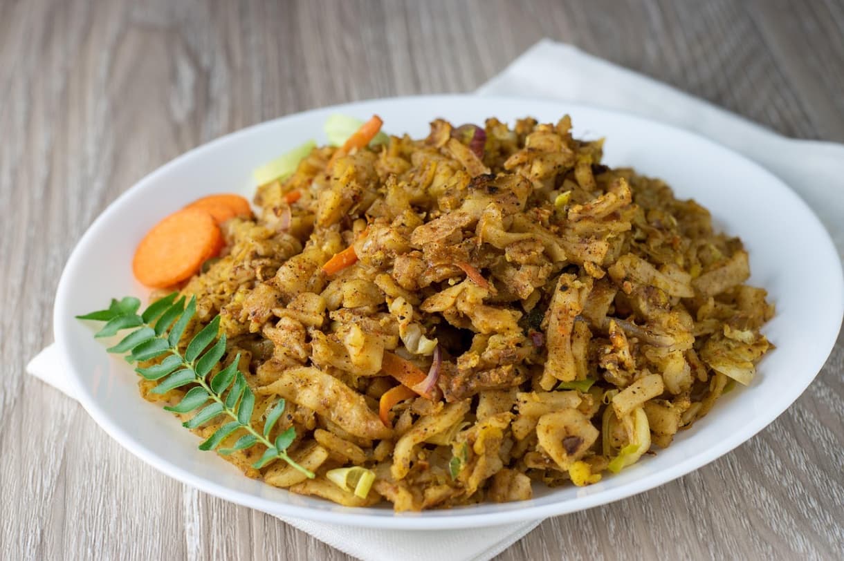 Plat typique de kottu, mélange de légumes et de pain frit, servi avec des carottes et des feuilles aromatiques