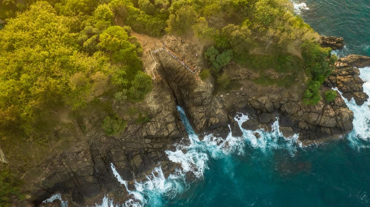 Vue aérienne d'une côte rocheuse avec des vagues, entourée de végétation luxuriante