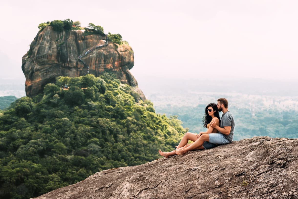 Couple amoureux admirant un paysage verdoyant au Sri Lanka, assis sur une roche.