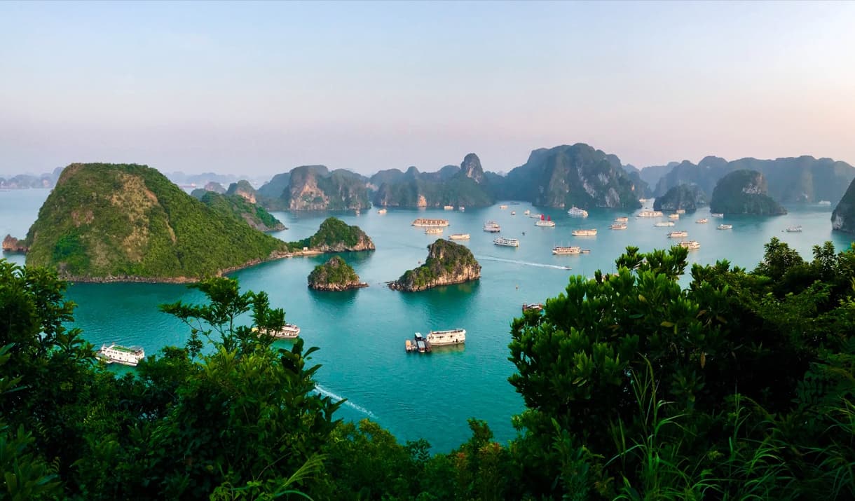 Vue panoramique de la baie d'Halong avec des îlots verdoyants et des bateaux pendant le coucher du soleil, Vietnam