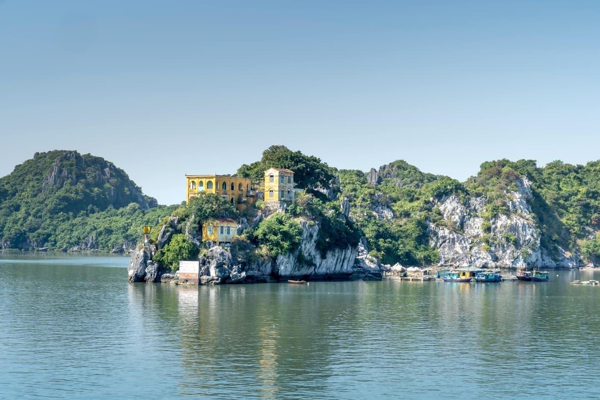 Île de Cat Ba avec bâtiments colorés et eaux calmes entourées de collines verdoyantes