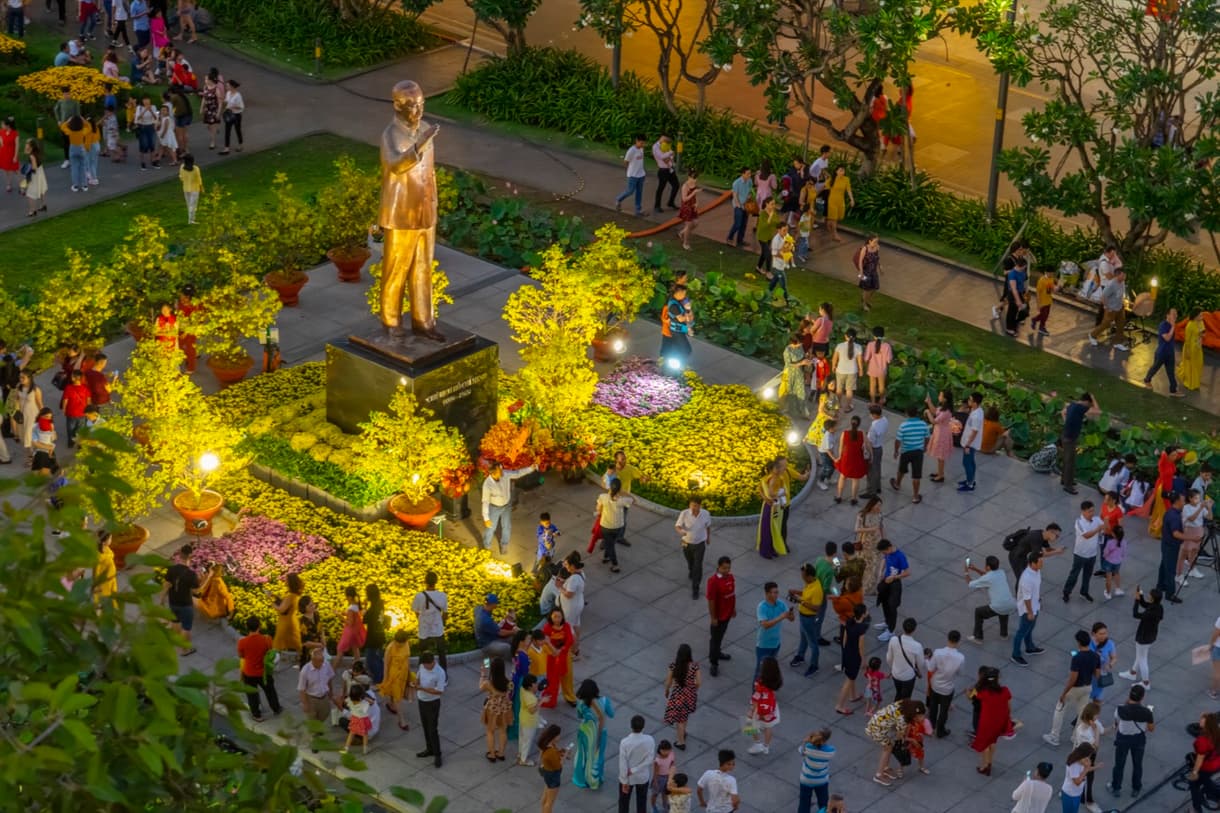 Statue de Ho Chi Minh illuminée sur Nguyen Hue Walking Street, entourée de visiteurs et de fleurs colorées.