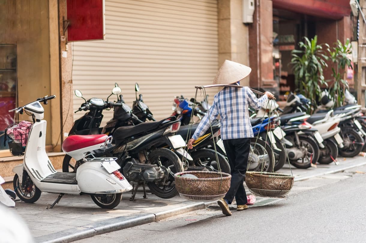 Femme avec un chapeau tissé traditionnel marchant entre des scooters au Vietnam