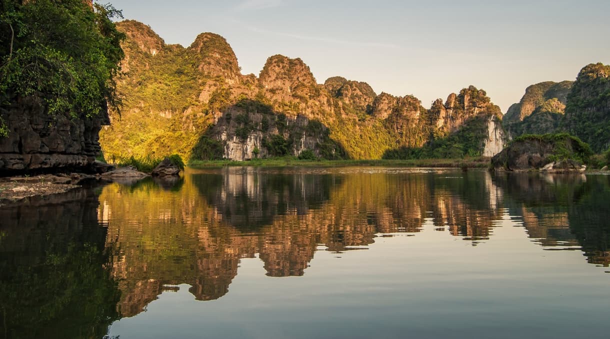Reflet des formations karstiques dans l'eau tranquille de Ninh Binh au coucher du soleil